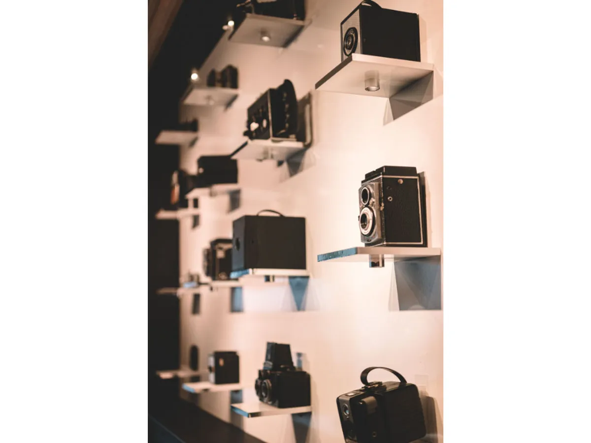 The scene highlights an interior with vintage cameras displayed on shelves along a wall, evoking nostalgia and creativity. The setting is ideal for photography exhibitions and art appreciation, emphasizing a connection to the hotel's role as home to a Pulitzer-winning photographic collection.