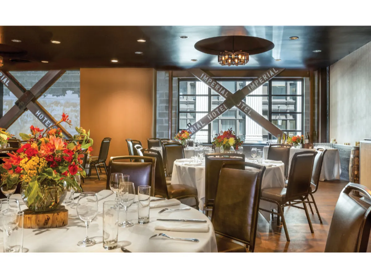 A sophisticated dining space filled with round tables dressed in white tablecloths, vibrant floral arrangements, and large windows that offer sweeping city views. The setting is elegant and tranquil, blending a sense of connection to the urban environment with a peaceful, restorative atmosphere.