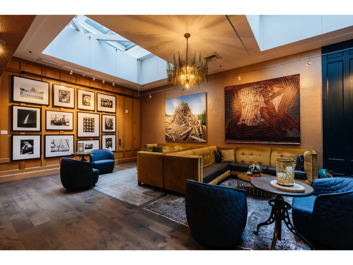 The scene features large, eye-catching artworks on the wall, a unique chandelier, and a plush seating arrangement that invites relaxation. The overall aesthetic is creative yet serene, suggesting a space where guests can unwind in style.