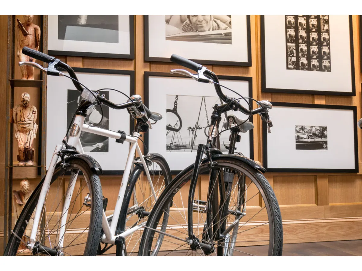This image captures a contemporary, creative hotel space featuring bicycles available for guests, black and white photographs that celebrate local art, and stylish wooden wall paneling. The atmosphere is vibrant and welcoming, suggesting opportunities for both activity and relaxation.