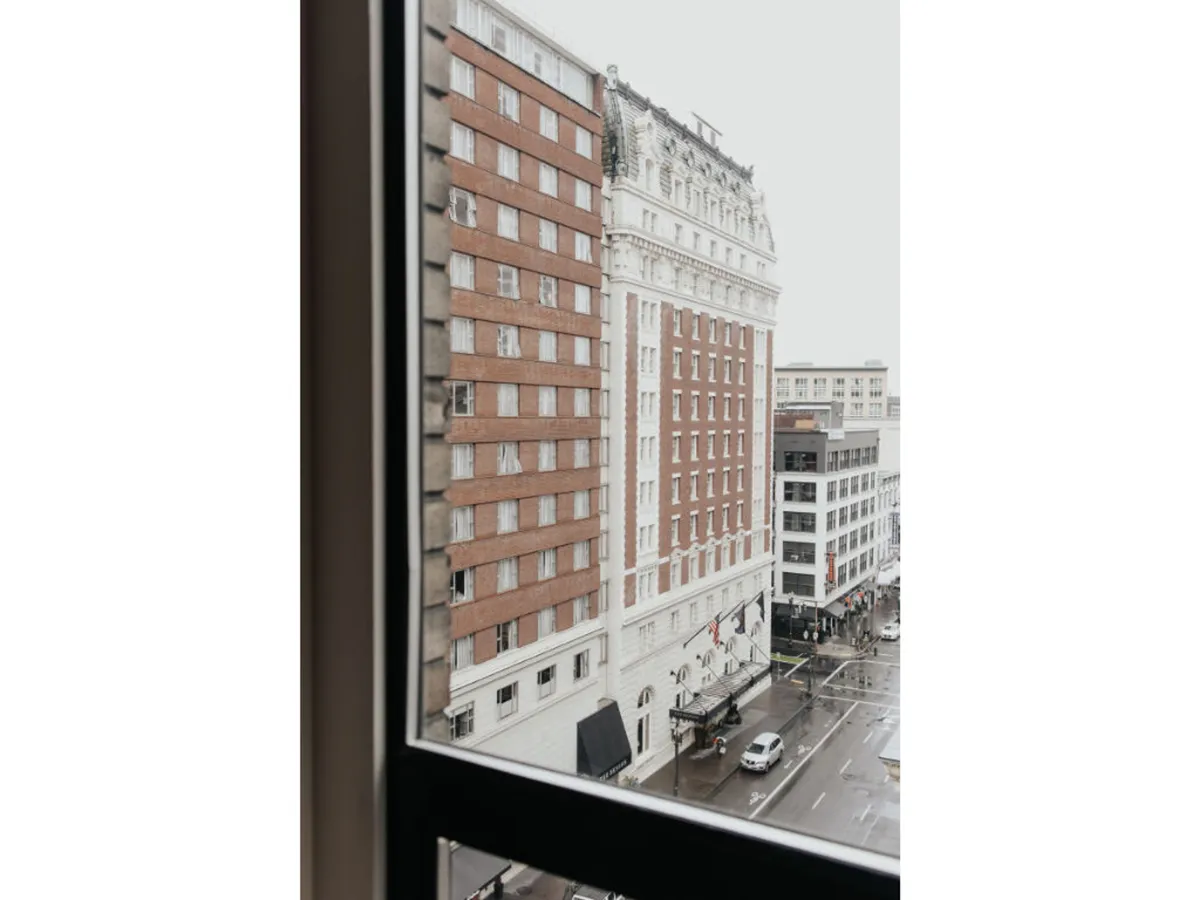 This image captures a rain-soaked Portland street scene featuring historical buildings, a vehicle, and a reflective pavement. The ambiance is tranquil, with people exploring the city, highlighting the beauty of Portland's historic architecture and urban life.