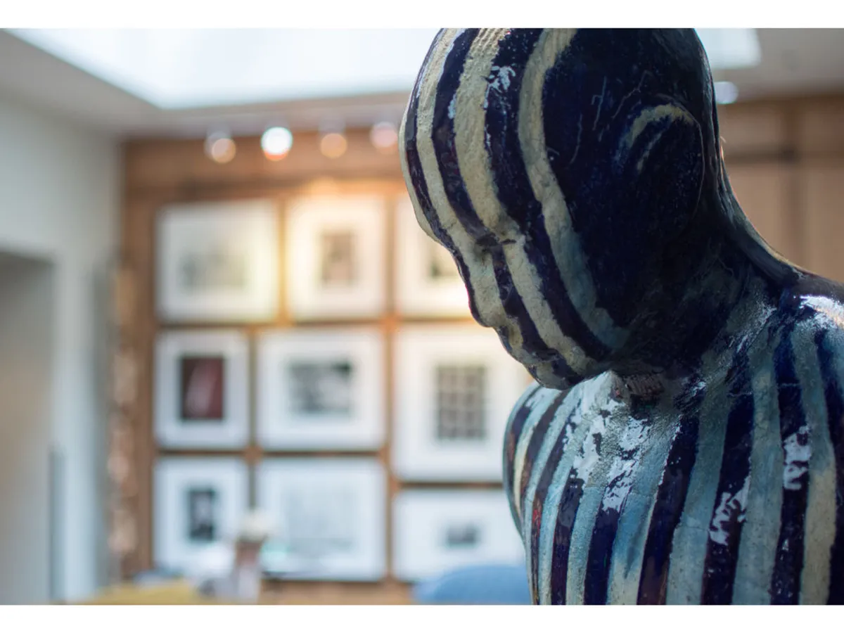 This thoughtfully curated interior features a striking sculpture and framed artwork along the walls. The mood is contemplative and inspiring, inviting viewers to experience unique art pieces and the interplay of light and shadow within the space.