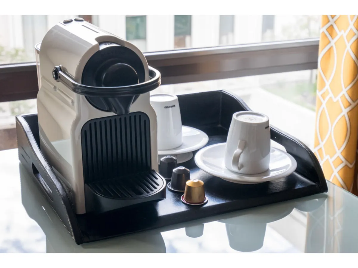This image shows a cozy interior with a prominent coffee machine, several neatly arranged coffee cups, and a tray, all beside a window. The space feels calm and welcoming, with gentle lighting and a sense of comfort.