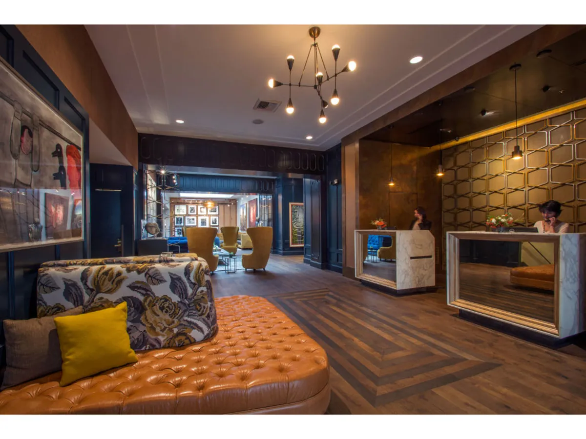 A chic hotel lobby with a tufted leather sofa, a modern reception desk, walls adorned with contemporary artwork, and distinctive lighting fixtures. The space exudes a blend of historic charm and boutique sophistication, welcoming guests to socialize or appreciate the artistic atmosphere.