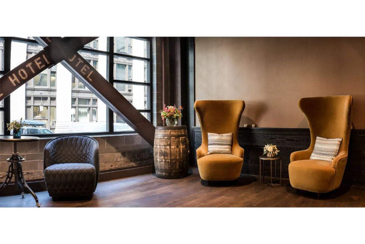 A cozy corner with two tall, stylish chairs, a barrel table, and a window providing city views. The relaxed atmosphere makes it an ideal spot for enjoying a drink, reading, or simply soaking in the urban surroundings.